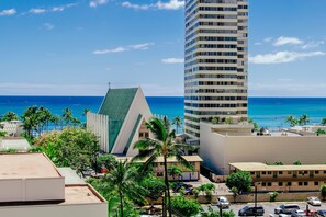 A high-rise building with a modern design, a parking area, and a view of the ocean. - Ocean-city Views Family Getaway at Waikiki Banyan Half a Block to the Beach (Honolulu)