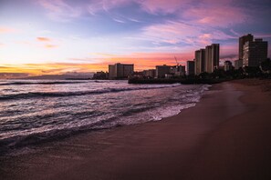 A beach with waves, a sunset, and high-rise buildings in the background. - Ocean-city Views Family Getaway at Waikiki Banyan Half a Block to the Beach (Honolulu)