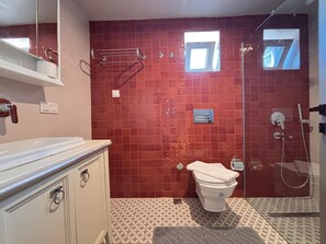A bathroom with a red-tiled wall, a toilet, a shower, and a sink with a cabinet. - Contemporary 1BR Stay in Historic Tophane (Istanbul)
