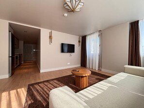 A hotel room with a bed, a TV mounted on the wall, a small round table, and a view of the kitchen and dining area through an open door. - Contemporary 1BR Stay in Historic Tophane (Istanbul)