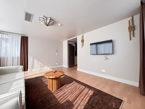A modern living room with a sofa, a round coffee table, a flat-screen TV mounted on the wall, and a wooden floor. - Contemporary 1BR Stay in Historic Tophane (Istanbul)