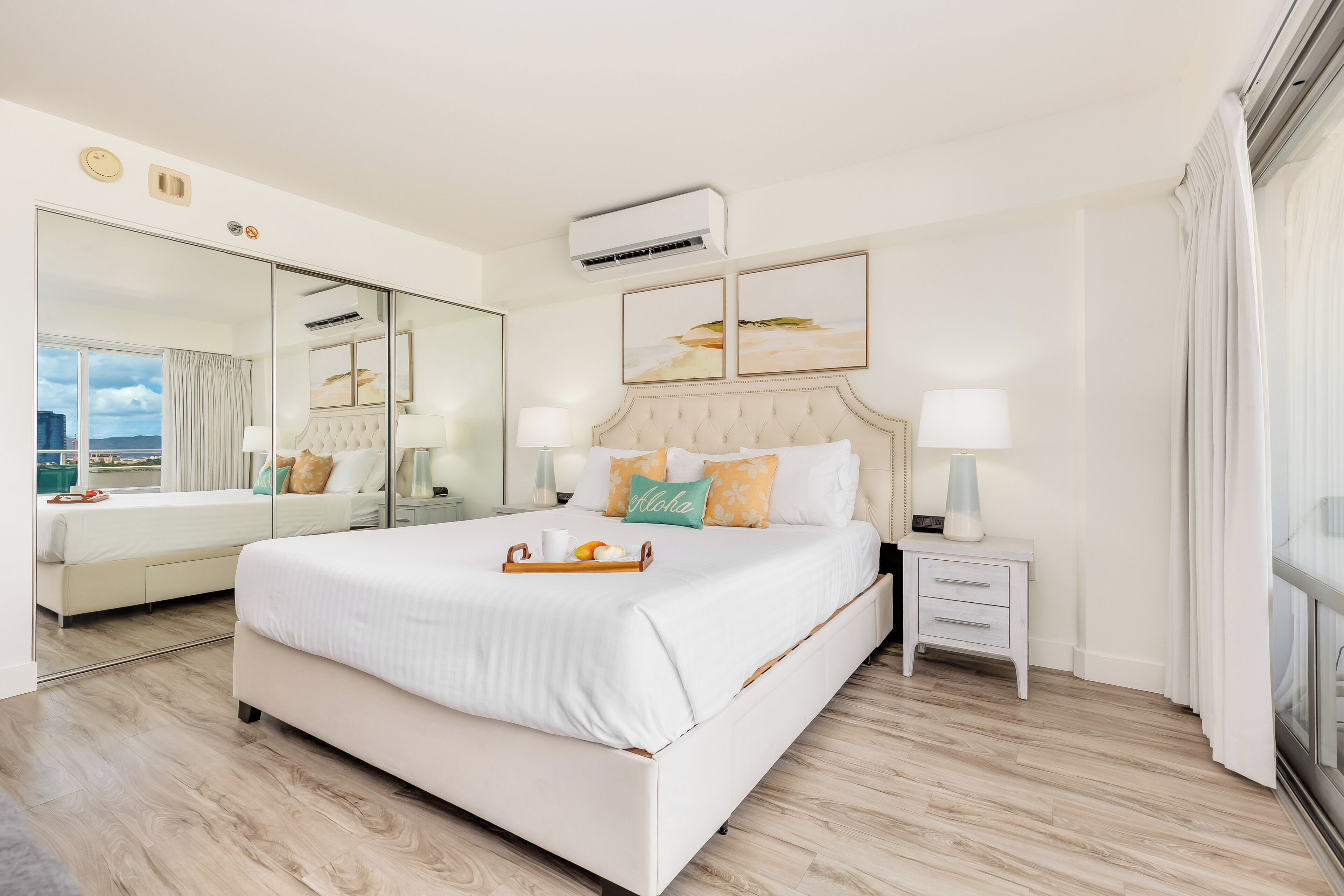 A modern hotel room with a large bed, bedside tables, a mirror, and artwork on the walls.