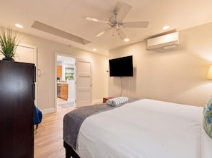A hotel room with a bed, a ceiling fan, a flat-screen TV, and an air conditioning unit. - Maui Kaʻanapali Condo - Ocean View, Walk to Beach (Lahaina)