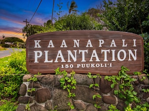 Een houten bord met de tekst 'Kaanapali Plantation 150 Puukoli'i' omringd door groen.