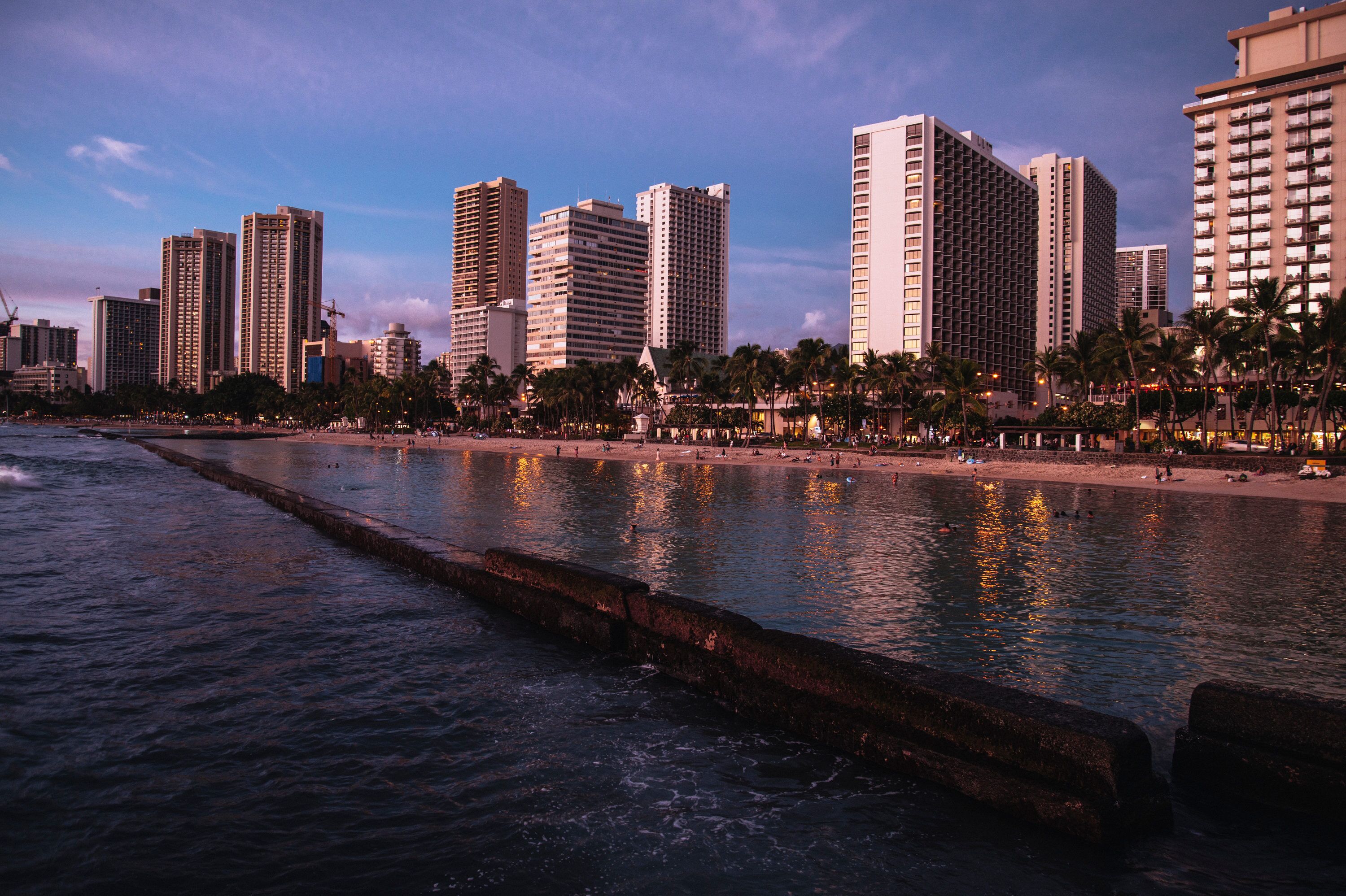 A coastal cityscape with high-rise buildings, a beach, and a seawall.