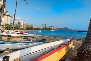 Uma praia com barcos, palmeiras e um horizonte urbano ao fundo.