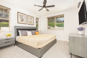 A bedroom with a bed, bedside tables, a ceiling fan, and large windows with a view. - Tranquil Vacation Home in Makaha Valley Near Beach W/exterior Dining & Bbq (Waianae)