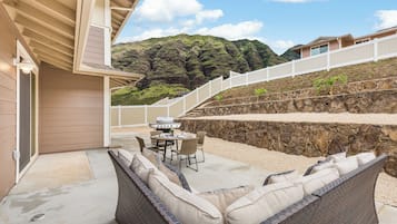 A covered outdoor patio with a stone wall, a grill, and wicker furniture.