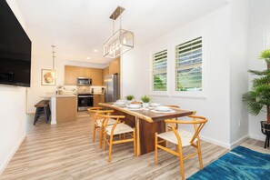 Une cuisine moderne avec des meubles en bois, des appareils en acier inoxydable et un coin repas comprenant une table et des chaises en bois.