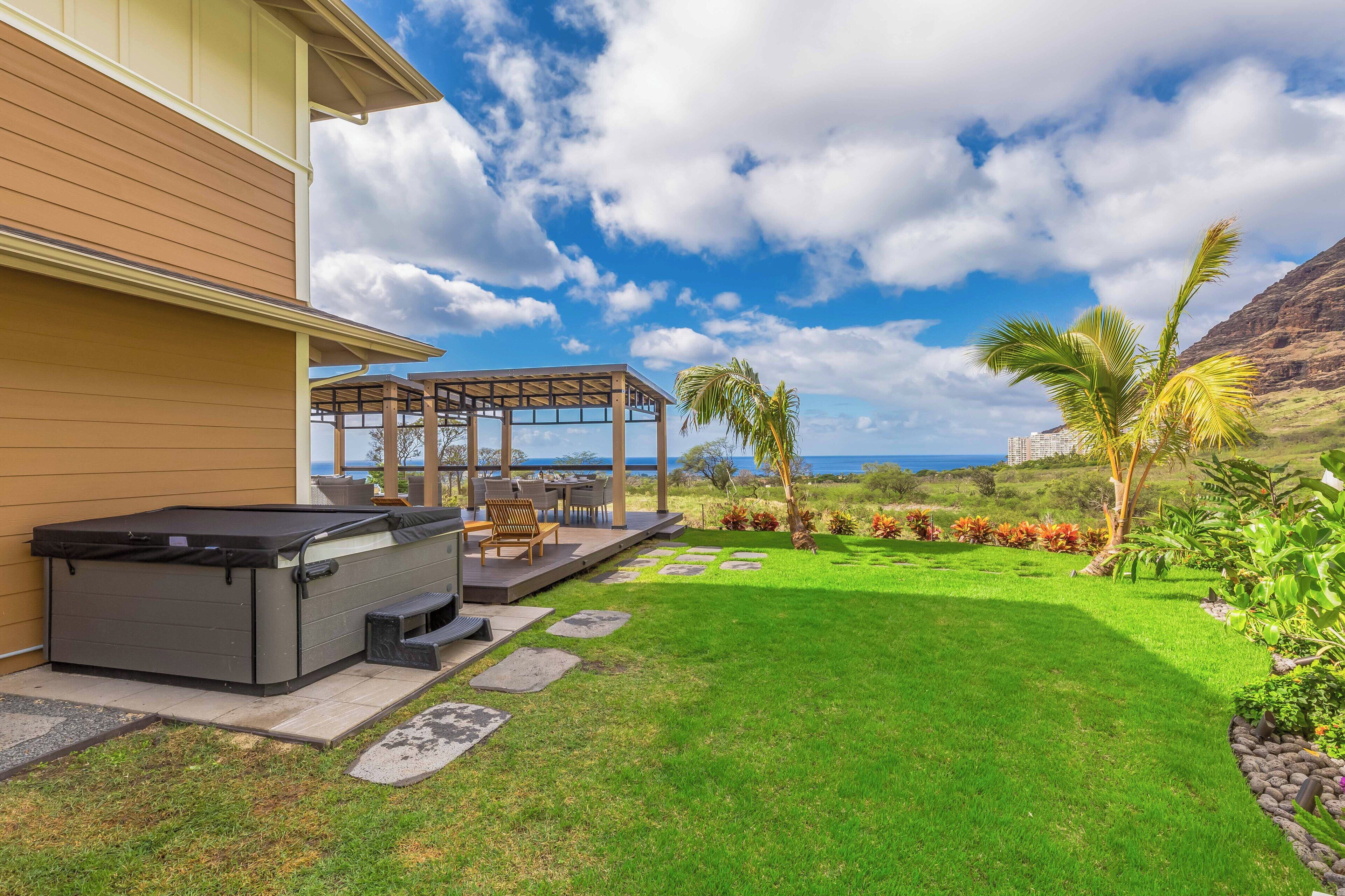 A modern outdoor patio with a hot tub, seating area, and a view of the ocean.