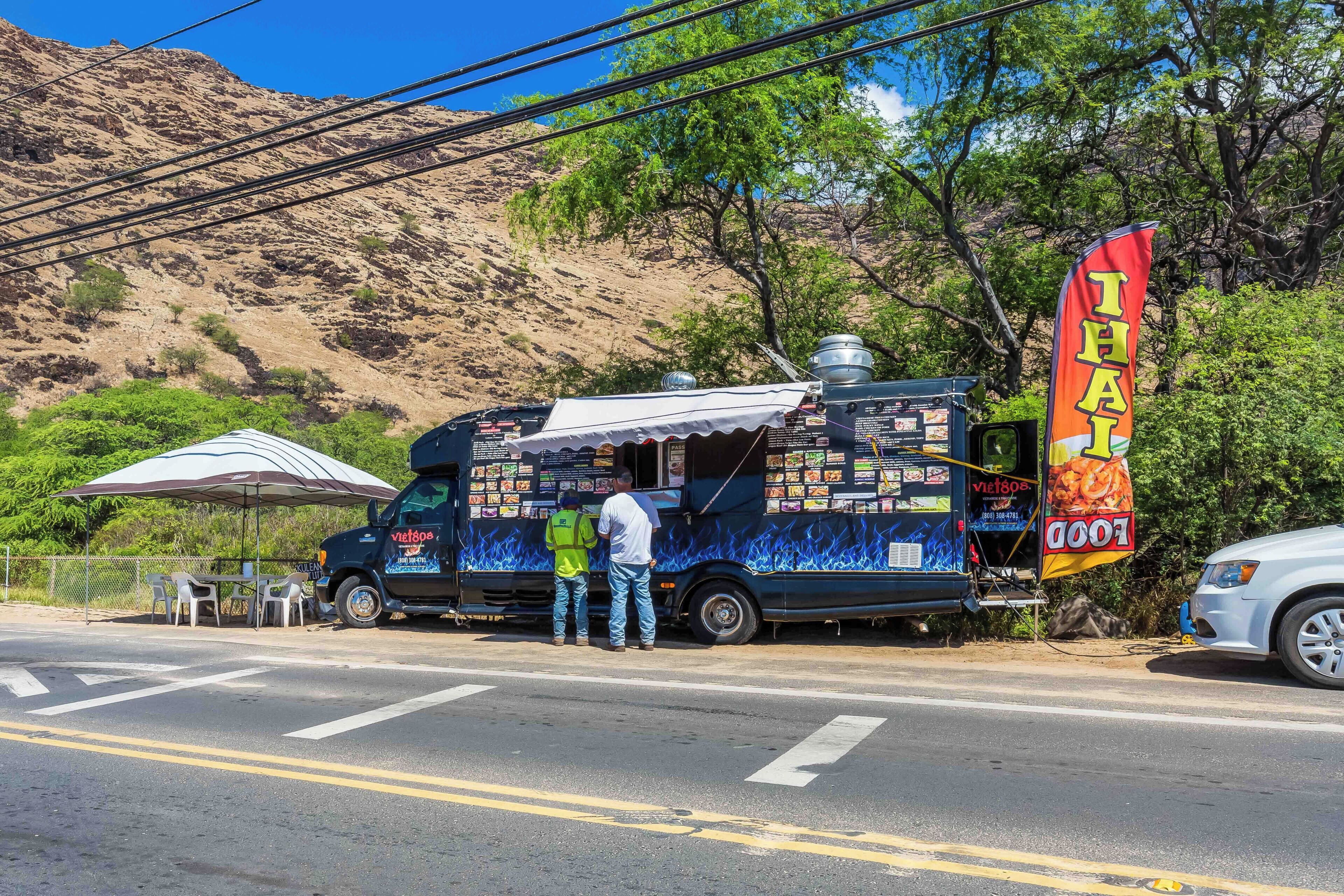 A food truck with a Thai food banner parked on a street.
