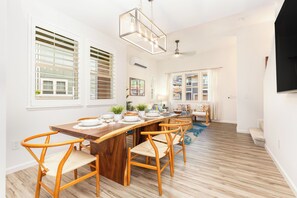 A modern kitchen with a wooden dining table, chairs, and a hanging light fixture. - Ocean View Home for Family Fun Getaway Near Beach W/hot Tub and Bbq Grill (Waianae)