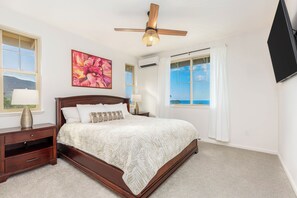 A bedroom with a wooden bed, two bedside tables, a ceiling fan, a large window with a view, and an air conditioning unit. - Ocean View Home for Family Fun Getaway Near Beach W/hot Tub and Bbq Grill (Waianae)