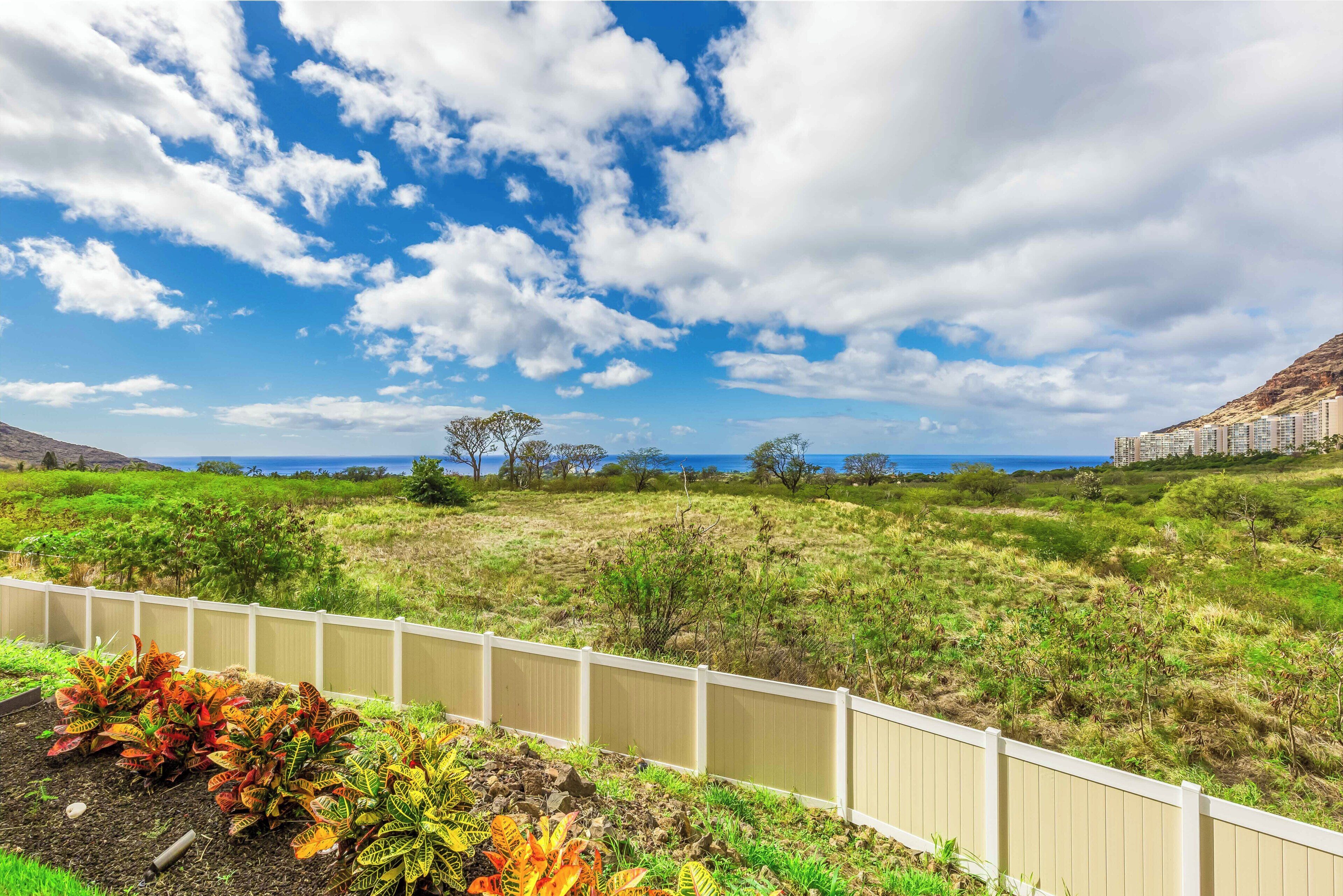 A coastal landscape with a white fence, green vegetation, and a distant view of buildings.