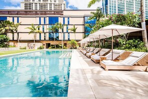 A swimming pool with lounge chairs and umbrellas, surrounded by palm trees and a building with multiple floors. - Ocean-city Exclusive Park Lane Condo by the Beach W/fabulous Amenities (Honolulu)