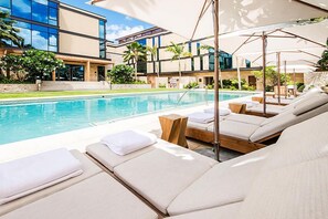 A poolside area with lounge chairs and umbrellas, a modern building in the background, and a clear blue pool. - Ocean-city Exclusive Park Lane Condo by the Beach W/fabulous Amenities (Honolulu)