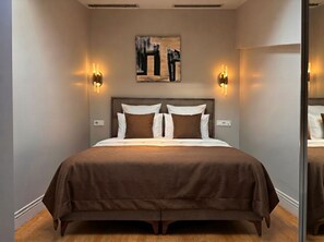 Une chambre d’hôtel moderne avec un grand lit, deux appliques murales et un tableau au-dessus du lit.