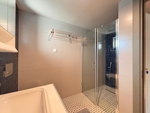 Un baño moderno con cabina de ducha de vidrio, una bañera blanca y suelo estampado.
