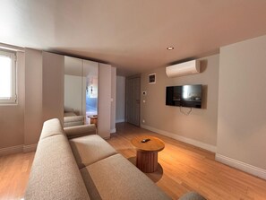 Un salon moderne avec un long canapé beige, une table basse ronde en bois et un téléviseur à écran plat fixé au mur.