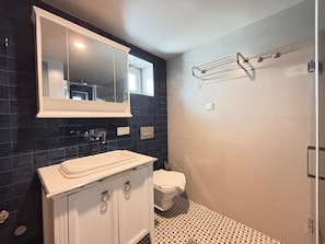 Une salle de bain avec un meuble-lavabo blanc, un miroir, des toilettes et un espace douche.