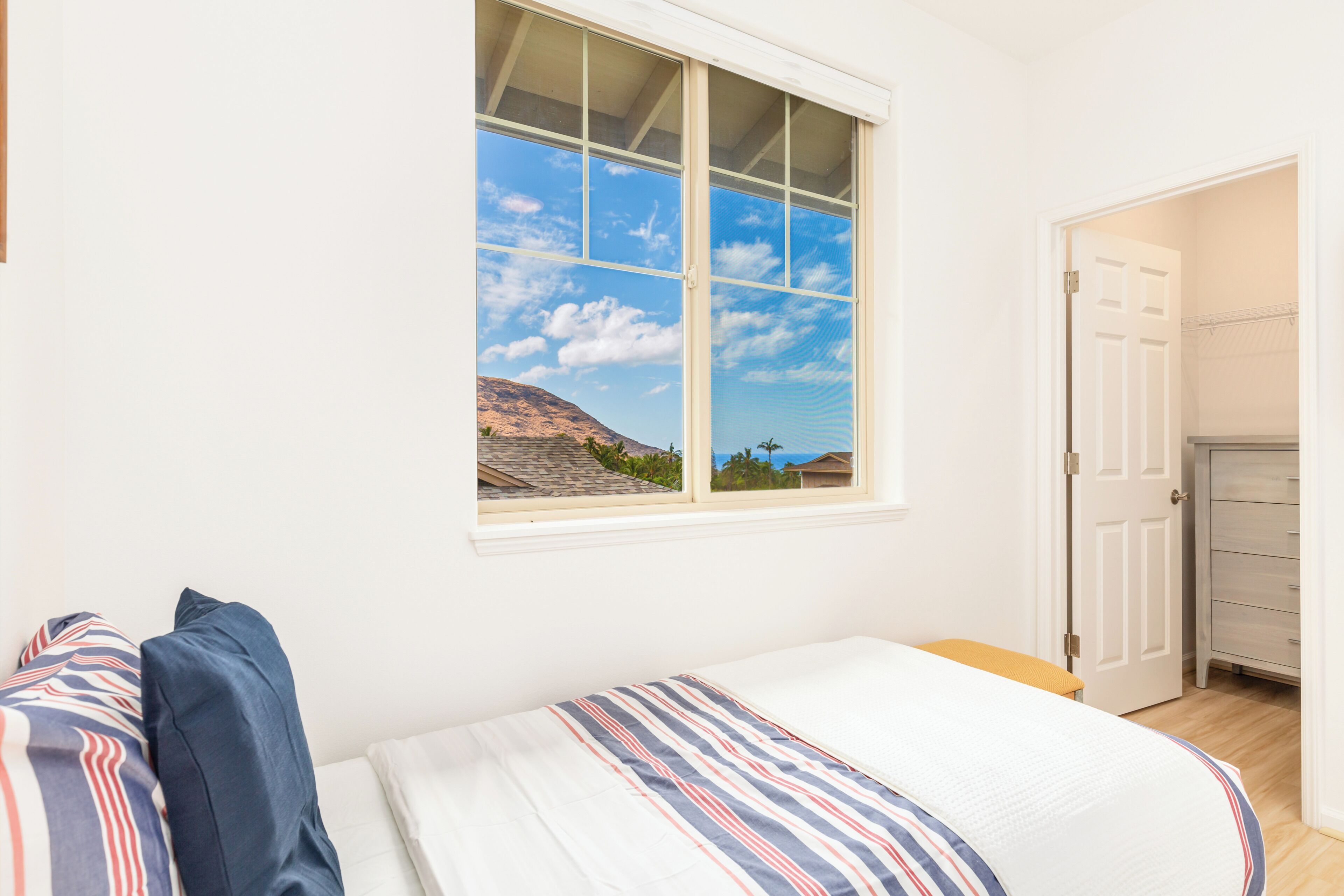 A bedroom with a bed, a window with a view of a mountain and palm trees, and a door leading to a closet.