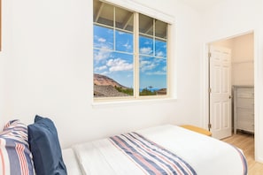 A bedroom with a bed, a window with a view of a mountain and palm trees, and a door leading to a closet. - Family Vacation Home W/ocean View at Makaha Valley in Secure Gated Community (Waianae)