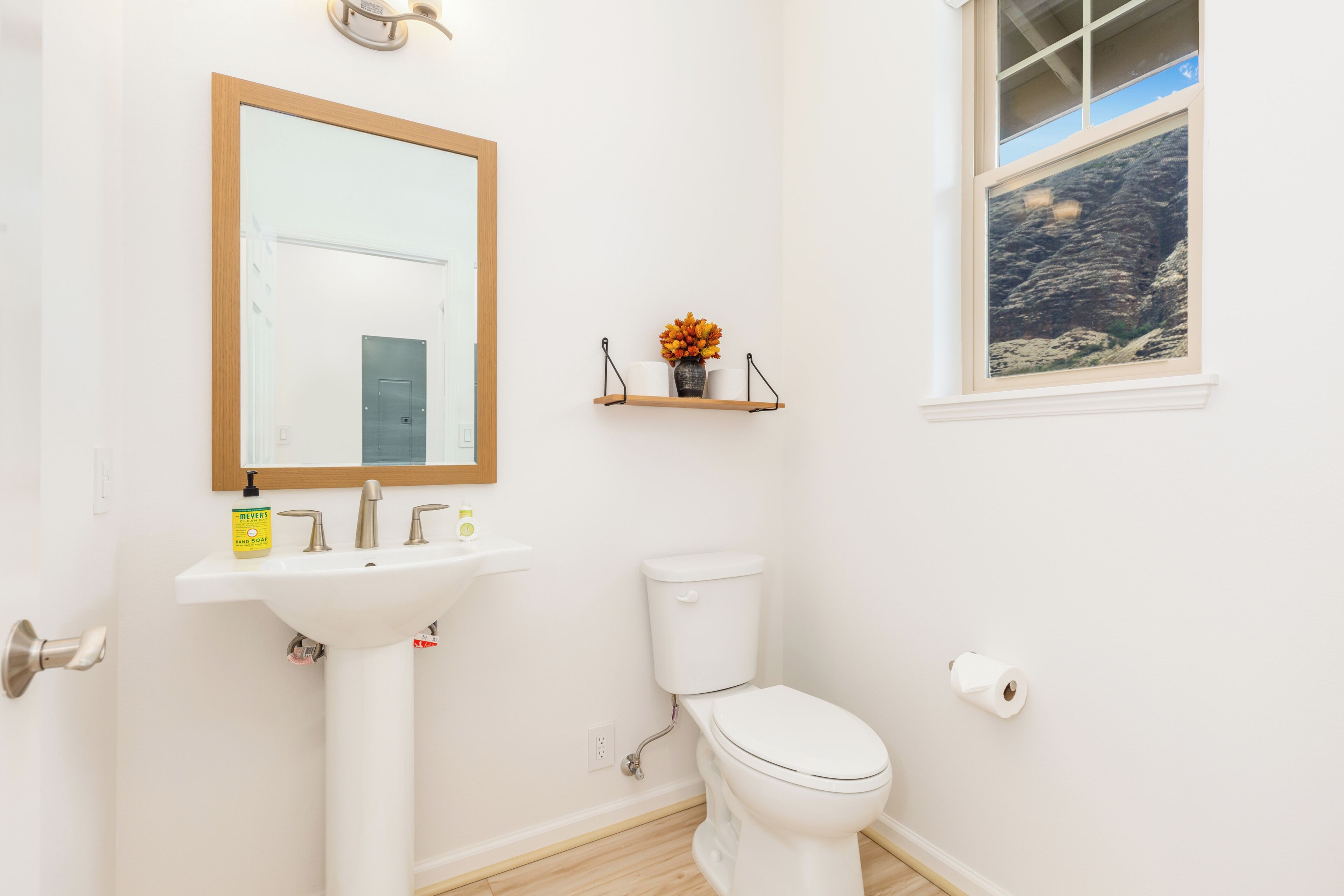 Un baño con un lavabo blanco, un inodoro, un espejo y una ventana con vistas a un paisaje rocoso.