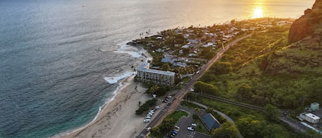 Vue aérienne d’une ville côtière avec une plage, une route et un immeuble à plusieurs étages.
