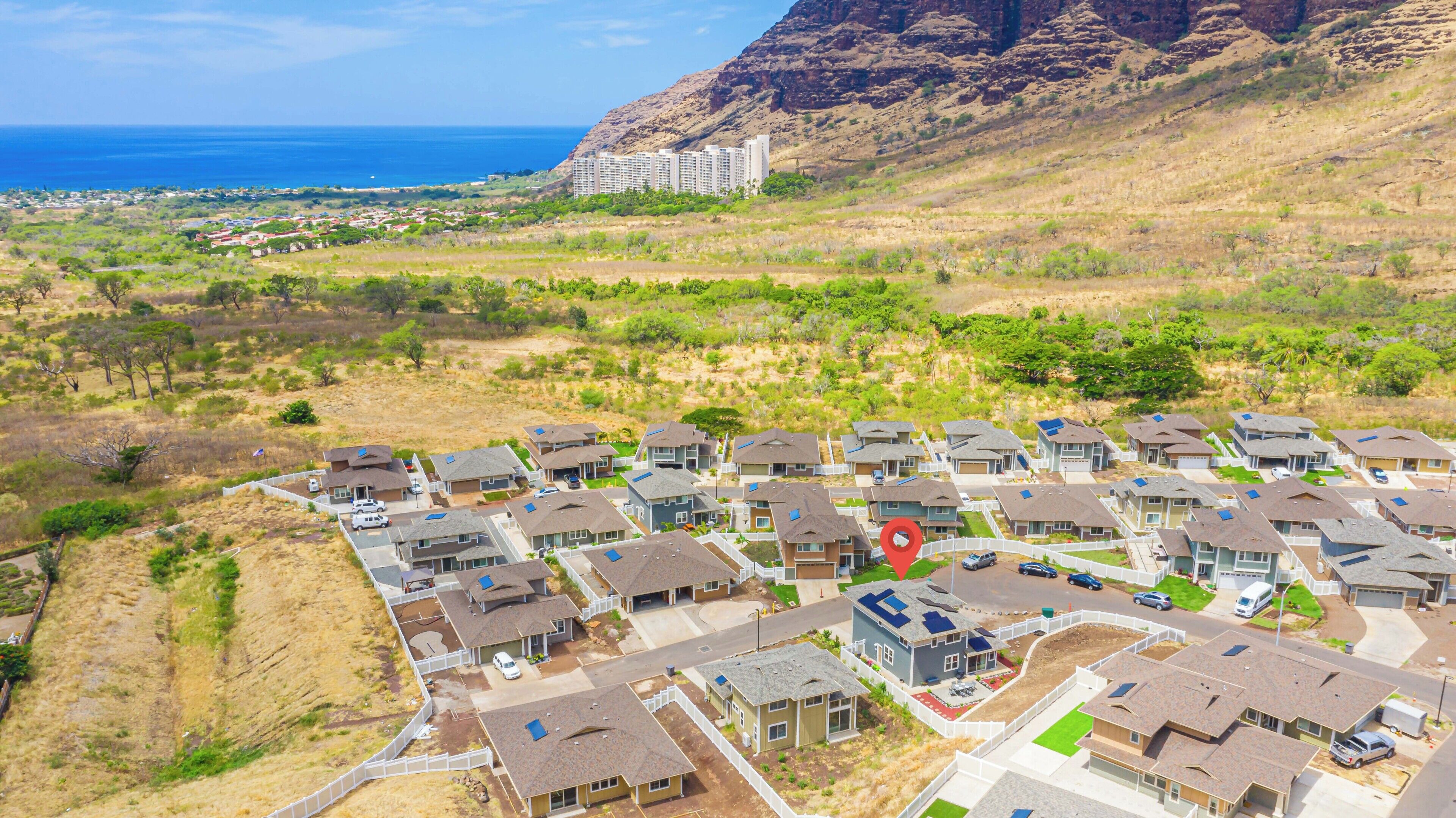 A residential area with houses, a road, and a view of the ocean and mountains in the distance.