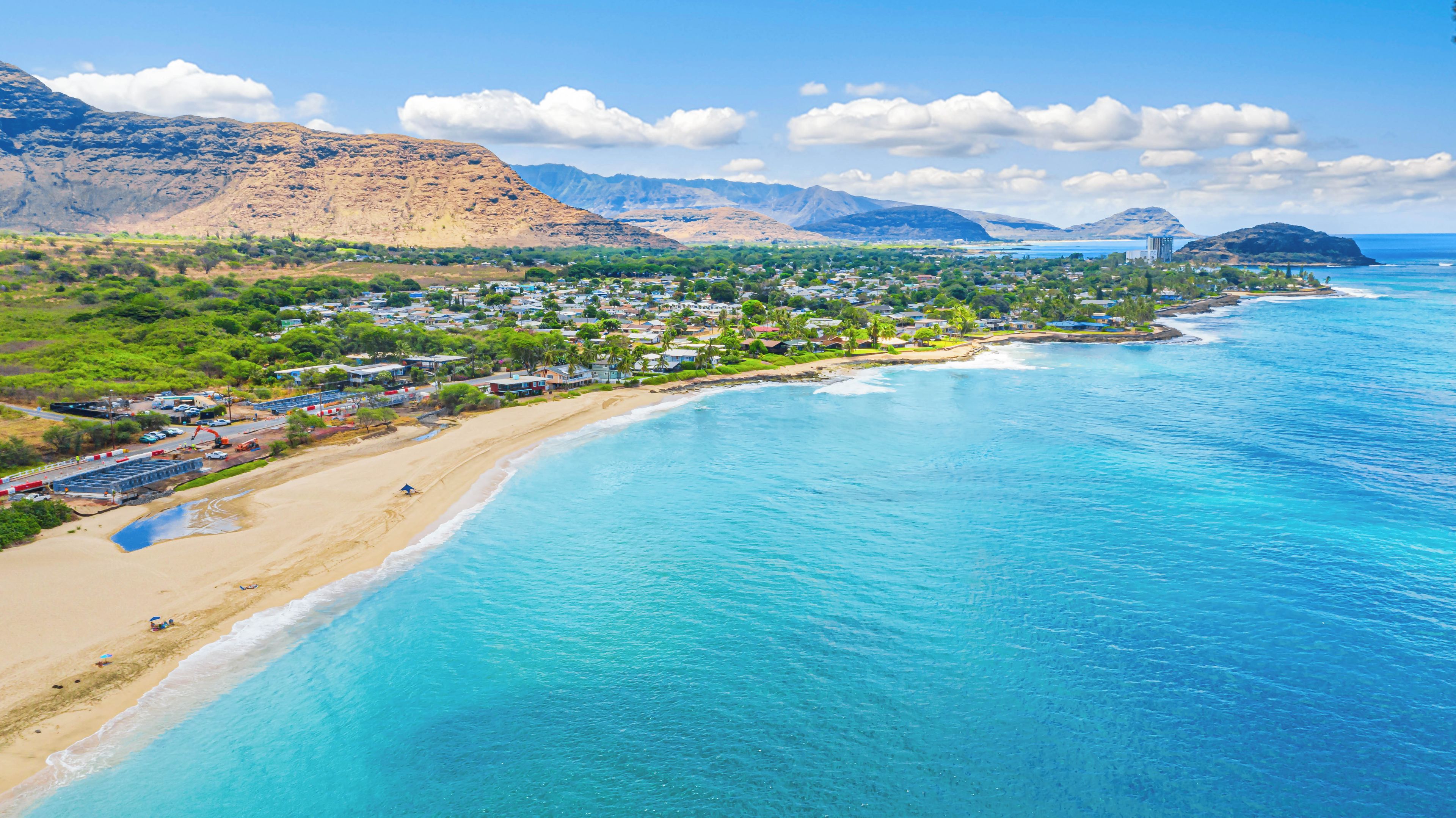 A coastal town with a beach, clear blue waters, and mountainous backdrop.