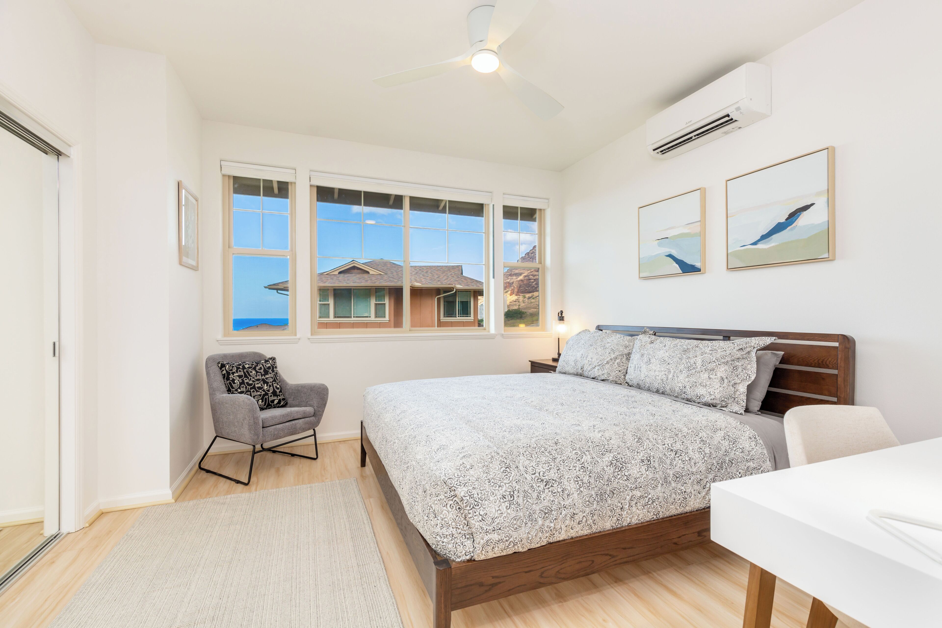 A bedroom with a bed, a chair, a desk, and a window with a view of a house.