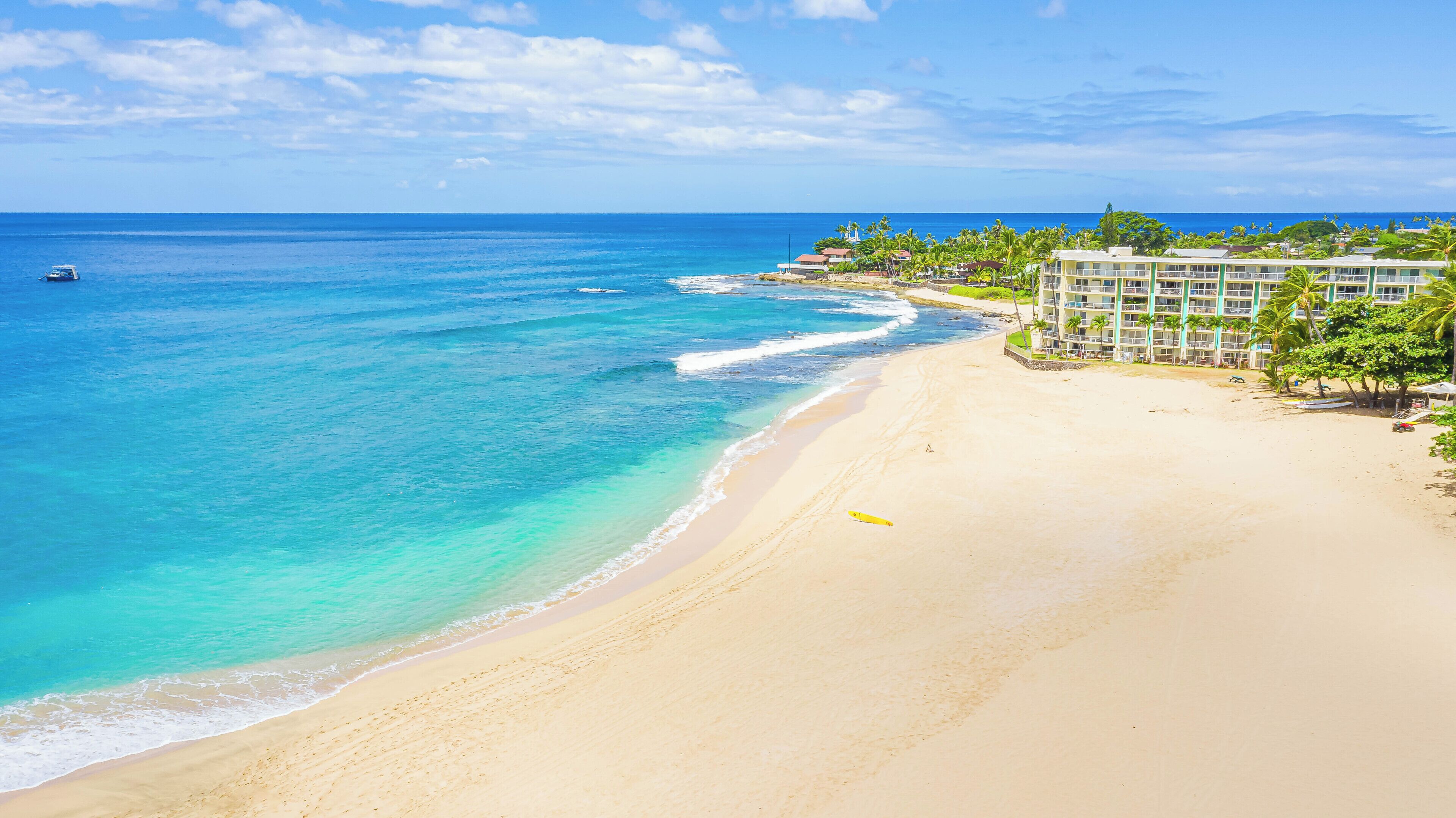 Une plage aux eaux turquoise et limpides, un rivage sablonneux et un bâtiment d’hôtel doté de plusieurs étages et de balcons offrant une vue sur l’océan.