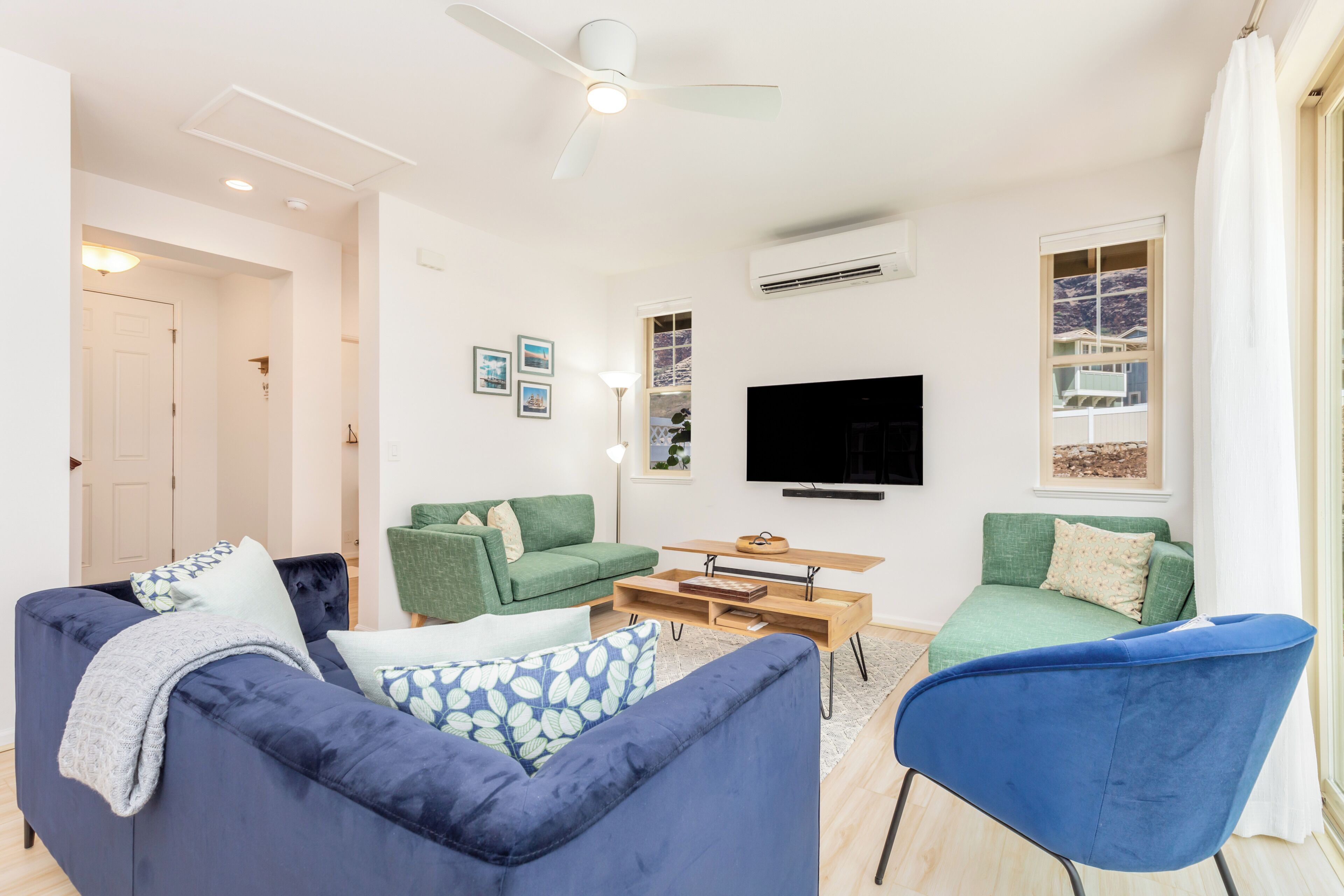 A modern living room with a ceiling fan, a flat-screen TV, and a large window with a view.