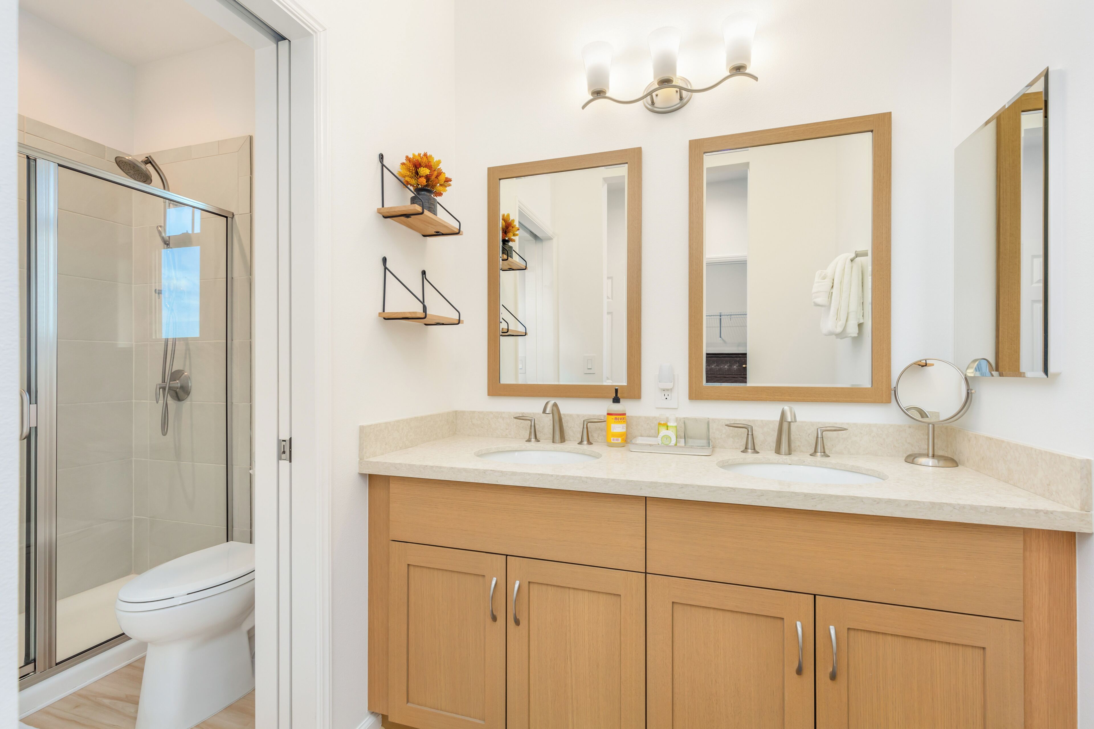 A modern bathroom with a glass shower enclosure, a double sink vanity with wooden cabinets, and two wall-mounted mirrors.
