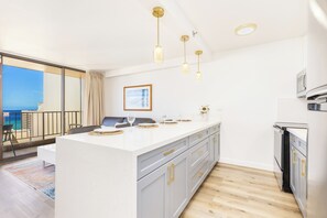 Een moderne keuken met een centraal eiland, hangende lampen en uitzicht op zee vanuit het balkon.