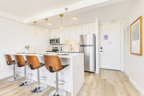 A modern kitchen with white cabinets, stainless steel appliances, and a central island with bar stools. - Unforgettable Waikiki Getaway/ocean & Diamond Head Views (Honolulu)