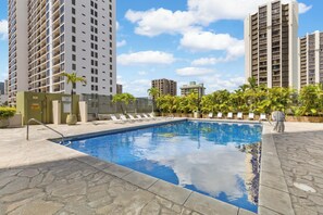 A swimming pool with lounge chairs and a safety sign, surrounded by tall residential buildings. - Unforgettable Waikiki Getaway/ocean & Diamond Head Views (Honolulu)