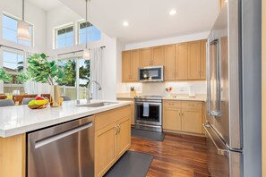 A modern kitchen with stainless steel appliances, wooden cabinets, and a large island. - Ocean-sunset Views Home in Gated Makaha Community W/great Amenities (Waianae)