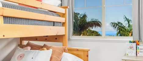 Un lit superposé avec vue sur les palmiers et l’océan, visible par une fenêtre.