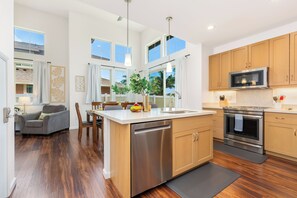A modern kitchen with a central island, stainless steel appliances, and wooden cabinets. - Ocean-sunset Views Home in Gated Makaha Community W/great Amenities (Waianae)