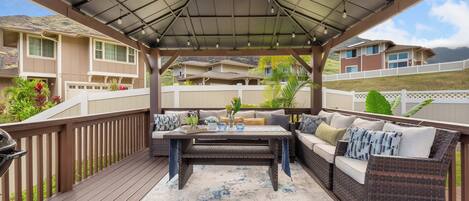 A covered outdoor patio with a wooden deck, a central table, and wicker furniture.