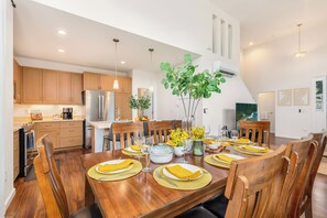 A modern kitchen with wooden cabinets, a stainless steel refrigerator, and a dining area set for six with yellow placemats and wooden chairs. - Ocean-sunset Views Home in Gated Makaha Community W/great Amenities (Waianae)