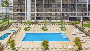 Ein Hotel mit großem zentralen Pool, mehreren Balkonen und einer gepflegten Außenanlage mit Liegestühlen und Pflanzen in Töpfen.