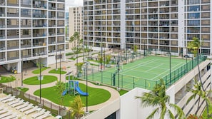 Ein mehrstöckiges Wohngebäude mit Balkonen, einem Tennisplatz und einem Spielplatz.