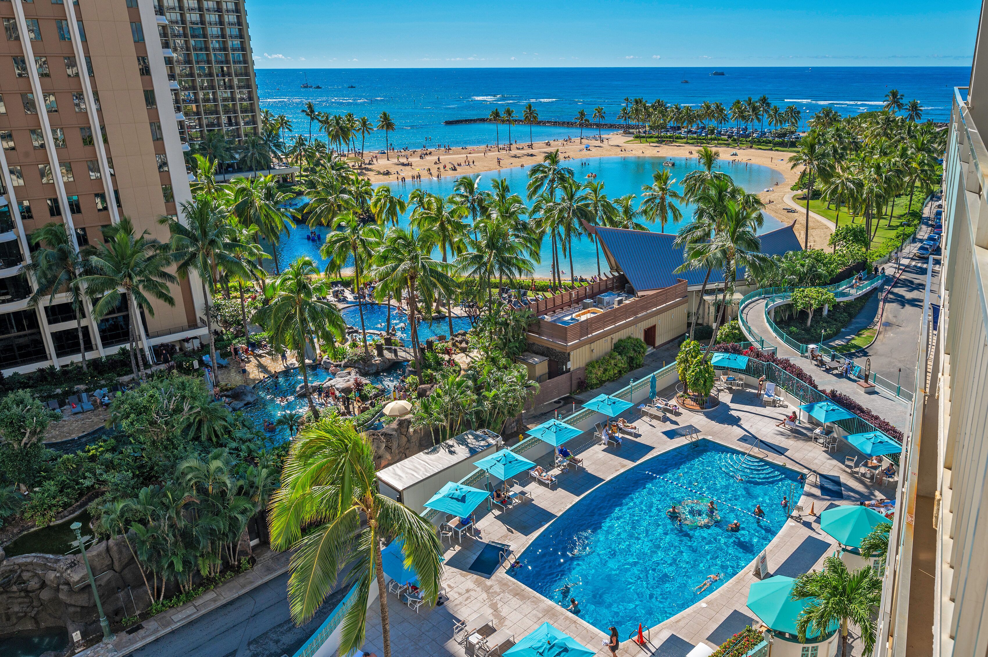 Un resort con varias piscinas, palmeras y vista al mar.