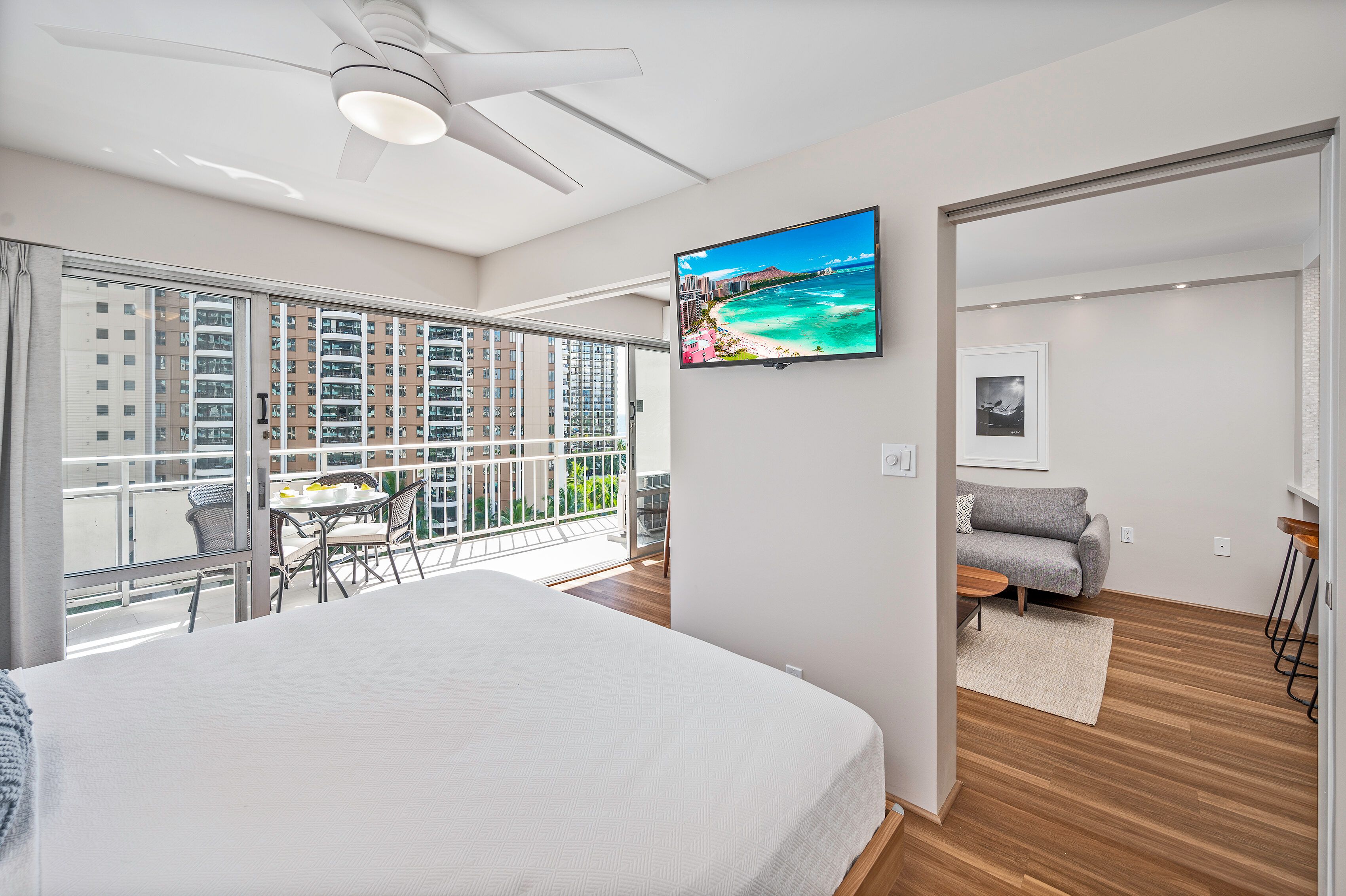 Een moderne hotelkamer met een groot bed, een balkon met een eethoek, een aan de muur bevestigde televisie en uitzicht op de stad.