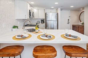 A modern kitchen with white cabinets, stainless steel appliances, and a central island with placemats and napkins. - Ocean-lagoon Condo W/full Kitchen at Ilikai Hotel and Steps to the Beach (Honolulu)