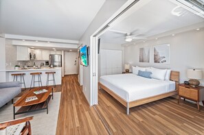 A modern hotel room with a large bed, a dining area with bar stools, a kitchen with a refrigerator, and a ceiling fan. - Ocean-lagoon Condo W/full Kitchen at Ilikai Hotel and Steps to the Beach (Honolulu)