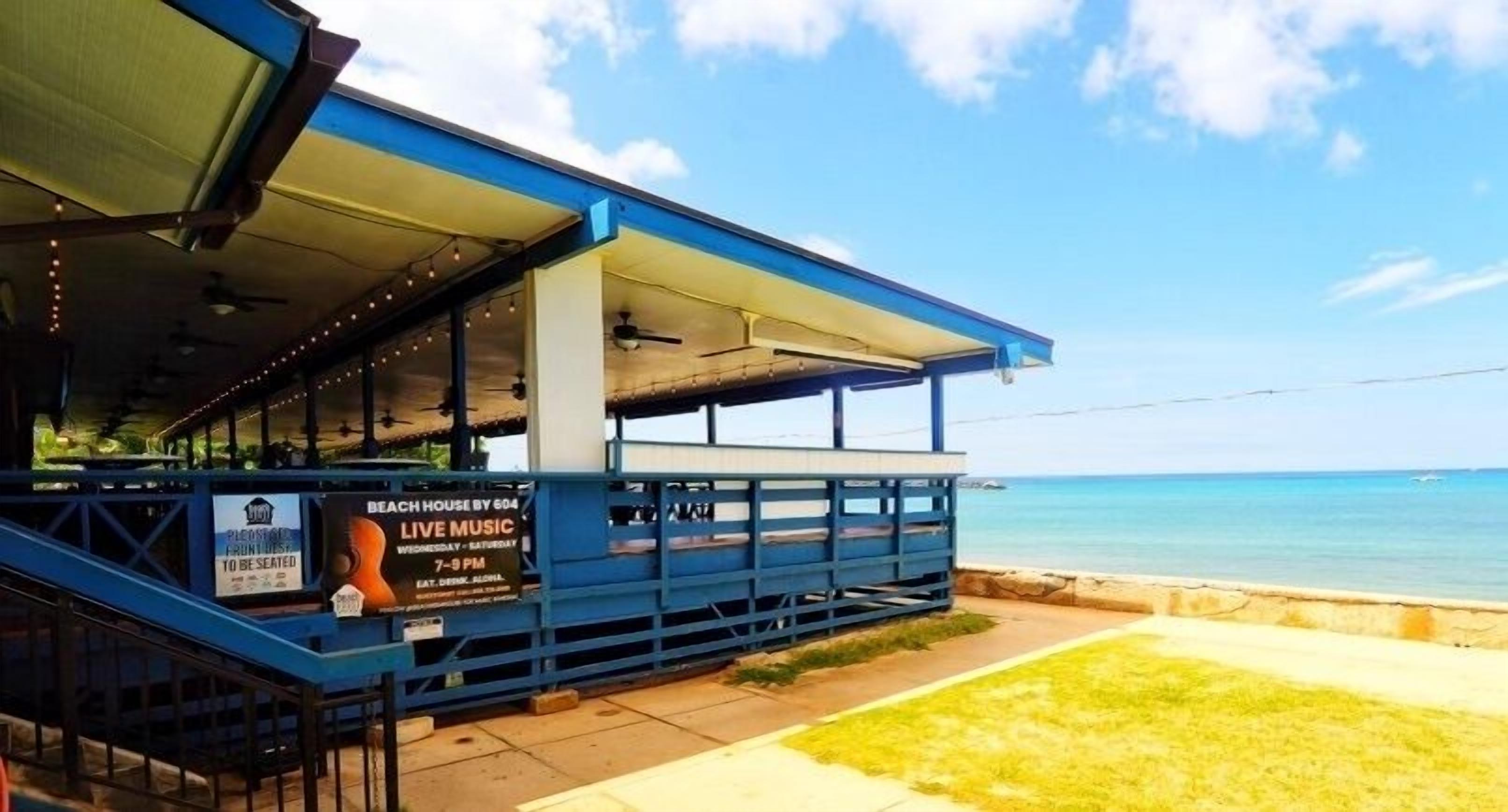 A beach house with a covered outdoor area, a sign advertising live music, and a view of the ocean.