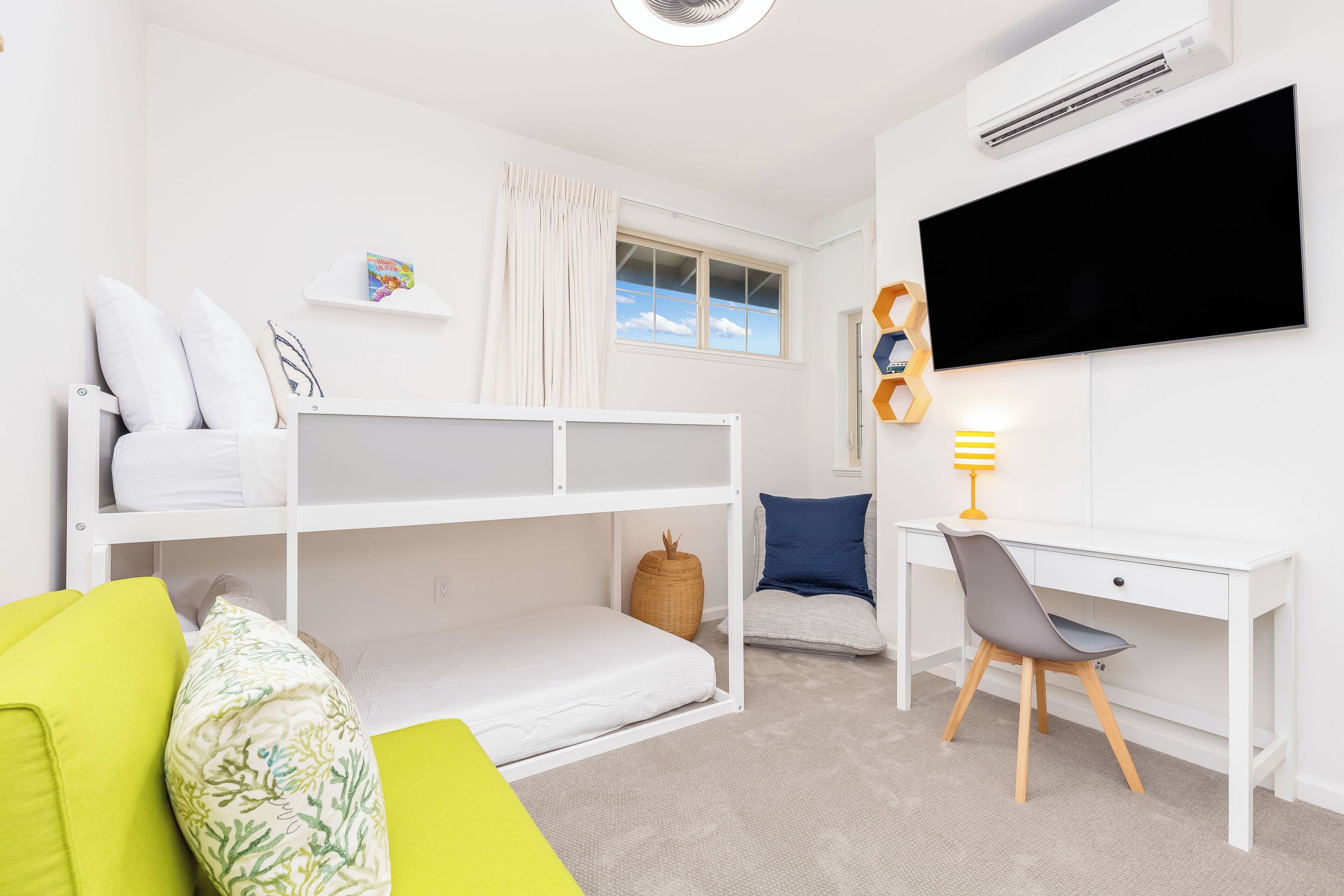 A child's bedroom with bunk beds, a desk, a chair, a TV, and a window with curtains.